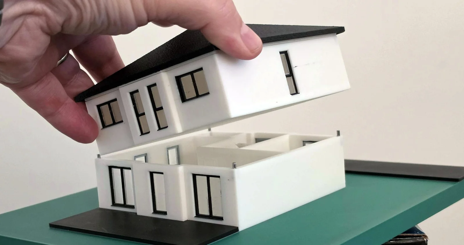 Hand hebt das Obergeschoss eines 3D-Hausmodells ab